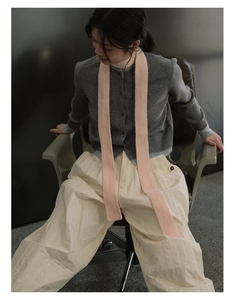 Detail of a pink knit wool scarf styled with a grey cardigan and cream wide-leg trousers