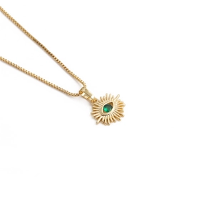 Detail of a gold necklace featuring a radiant sun pendant with a green gemstone center