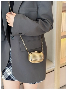 Close-up of golden metallic mini suitcase bag with chain strap worn by a female model