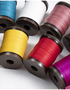 Detail view of 0.4mm round waxed threads in various colors on vintage brown spools