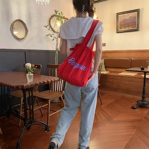 Detail of red drawstring canvas tote bag with Bonjour print worn by a model in a cafe