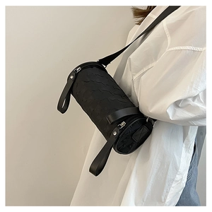 Detail of black cylindrical crossbody bag with textured pleated fabric on a model