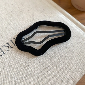 Close-up of black wavy flocked hair clip with soft matte texture on linen background