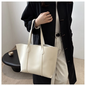 Minimalist cream tote bag in soft synthetic leather held by a person in a modern interior