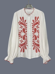 Dettaglio ricamo floreale su camicia in cotone bianco a maniche lunghe con volant
