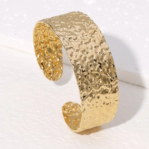 Macro detail of golden irregular hammered texture on stainless steel wide open cuff bangle