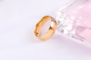 Close-up of polished gold wide band ring displayed with a pink perfume bottle