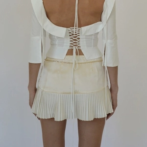 Detail of cross tie-back white top and beige pleated mini skirt with pearl waist chain