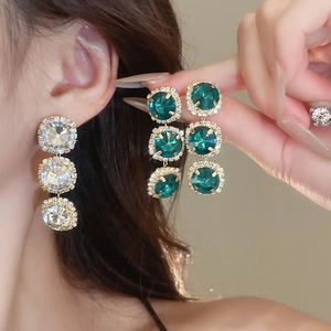 Close-up of gold earrings with green and white square stones on model