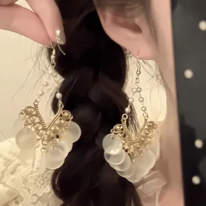 Détail de boucles d'oreilles vintage avec perles blanches et disques givrés sur un modèle