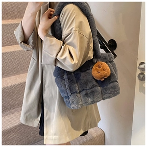 Cold grey plush shoulder bag with brown bear pendant worn by a model in soft lighting