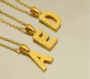 Macro detail of three 18K gold stainless steel letter pendants with unique hammer textures