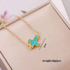 Detail view of a 2cm gold cross necklace with turquoise inlay in a beige jewelry box