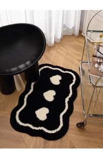 Detail of black plush heart bath mat with white wave border on wooden floor