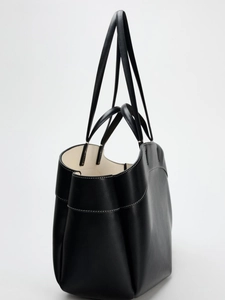 Side view of black faux leather tote bag with white contrast stitching and dual handles