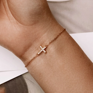 Close-up of gold cross charm bracelet set with small stones worn on a female wrist