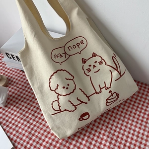 Flat lay of a white canvas tote bag with cute pet illustrations on a plaid tablecloth