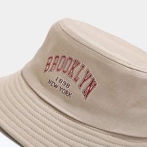 Detailed macro view of a beige bucket hat with vintage Brooklyn 1898 New York embroidery.