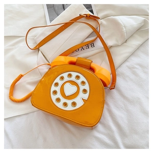 Macro shot of orange patent leather crossbody bag in vintage rotary telephone shape