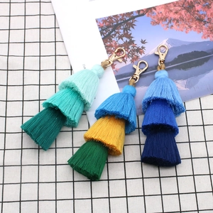 Three handmade colorful cotton tassel keychains with metal clasps on a grid background