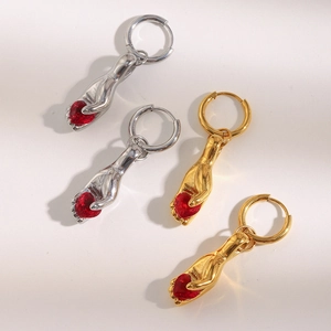 Detail view of gold and silver hand-shaped earrings holding red heart gemstones