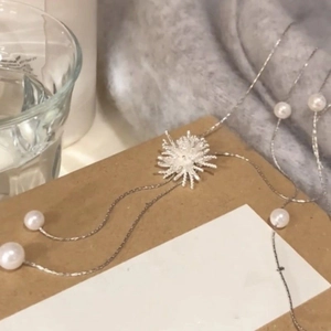 Détail du collier à pendentif soleil argenté avec perles blanches sur fond en tricot gris