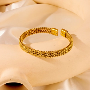 Detail shot of golden braided mesh bracelet with polished square ends on silk background