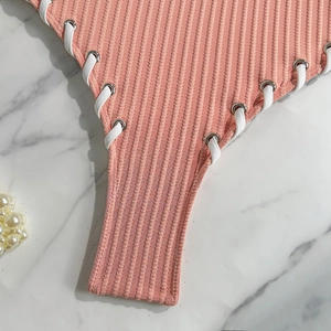 Detailed view of pink ribbed swimsuit fabric with white side lace-up and silver eyelets