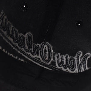 Macro shot of white cursive embroidery detail on a black cotton baseball cap surface