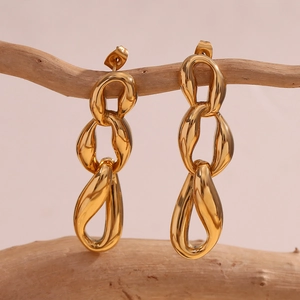 Macro view of gold-plated triple link chain earrings hanging on a natural branch