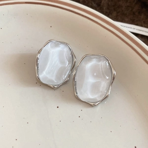 Detailed view of silver-framed oval earrings with white marble resin inserts on a ceramic plate