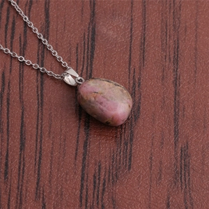 Macro view of polished round rhodonite stone pendant with silver chain on wood