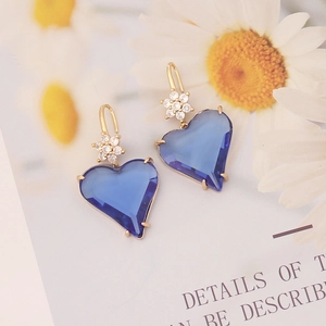 Detail view of deep blue heart earrings with golden flower hook on a floral background
