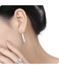 Detail of silver sword earring with zircons and irregular texture wide ring worn by model