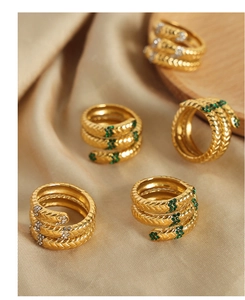 Details eines goldenen Schlangenrings mit grünen Kristallen auf Champagner-Satin