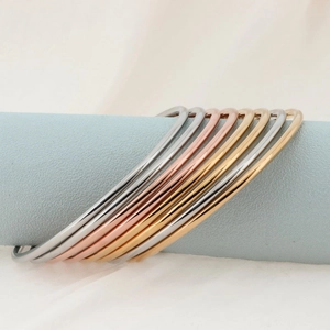 Polished 18k gold and silver stainless steel bangles displayed on blue cylindrical stands