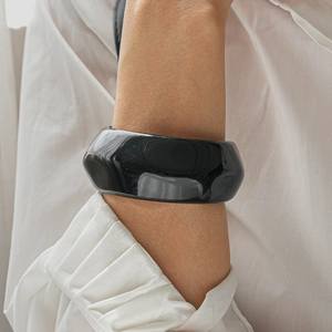 Detail of glossy black wide resin bangle with irregular fold texture on wrist