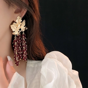 Detail of vintage gold leaf earrings with dark red beaded tassels on a model