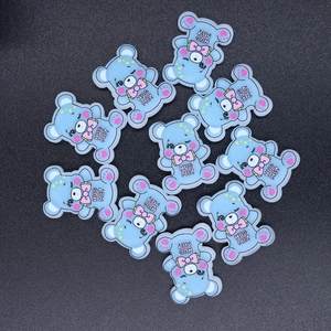 Flat lay of blue resin bear charms with pink bowties and Hug Me text for DIY crafts