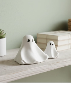Detailopname van twee witte keramische spookbeeldjes met een matte afwerking op een plank