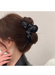 Dettaglio di uno scrunchie in raso nero lucido fissato su una pettinatura a chignon