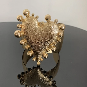 Close-up of golden wide open cuff bracelet with hammered heart and bead detailing