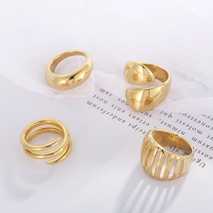 Flat lay of four minimalist gold-finish metal rings with varied hollow and twisted textures