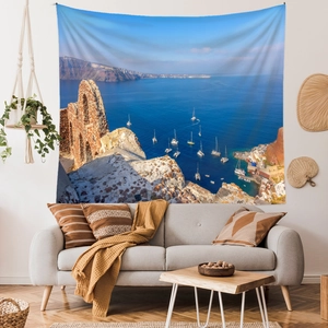 Santorini landscape tapestry hanging on a living room wall over a modern grey sofa