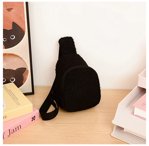 Close-up of black plush crossbody bag on a wooden table in a warm home setting