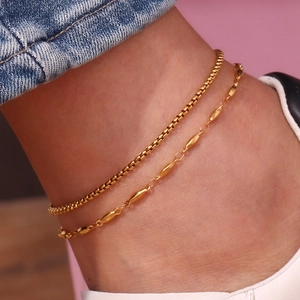 Detailed macro view of layered gold box chain and beaded anklet on a female ankle