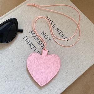 Pink heart-shaped leather pendant accessory styled with sunglasses and an open book
