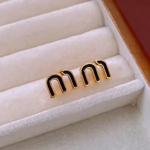 Elegant gold M-letter stud earrings with black enamel inlay in a white jewelry box