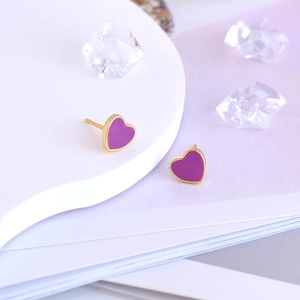 Macro shot of gold and purple heart-shaped stud earrings with glossy enamel finish