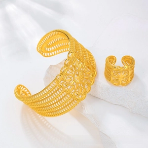 Detailed close-up of golden hollow flower bangle and matching ring set on white stone